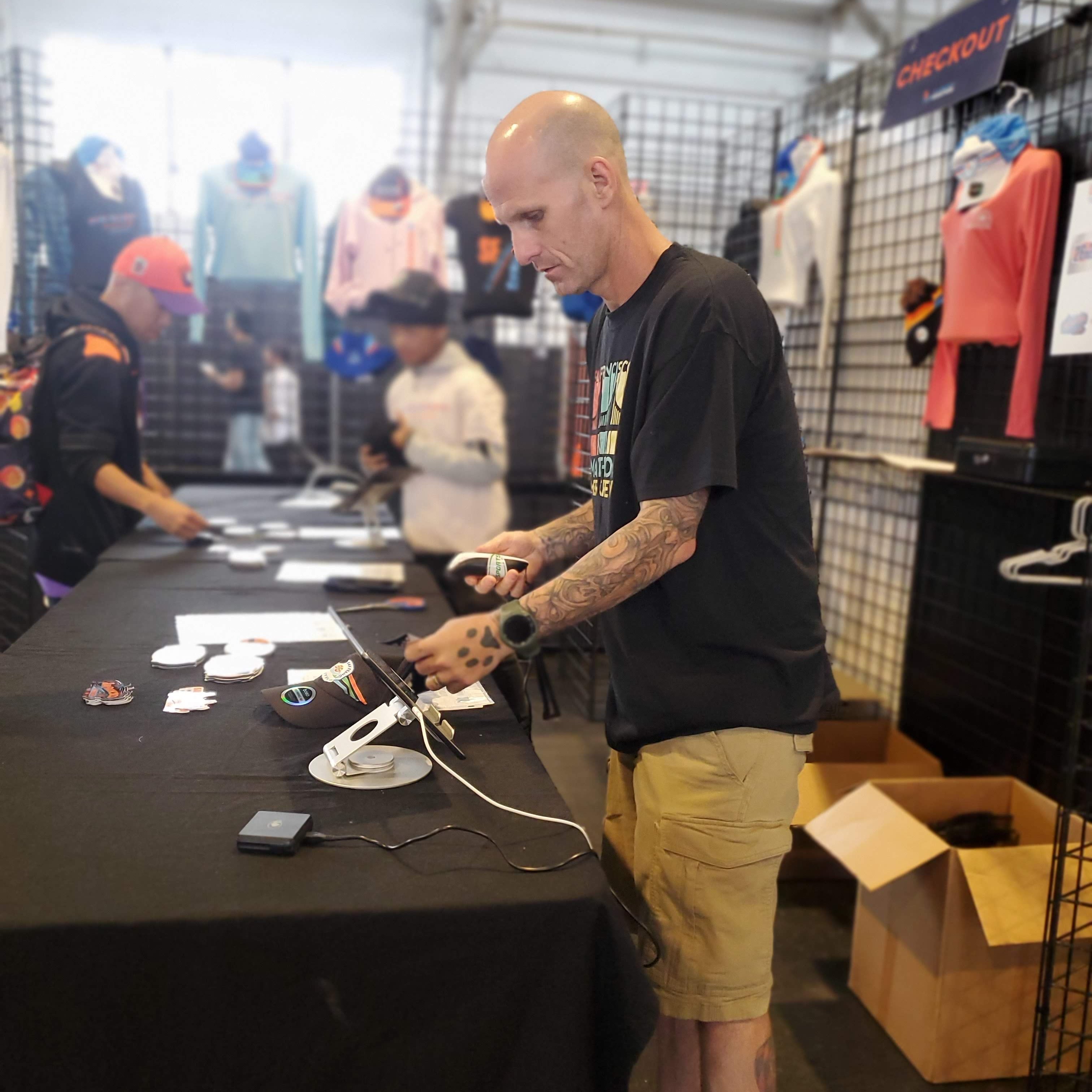 Man working on a register at a convention booth with other attendees in the background.